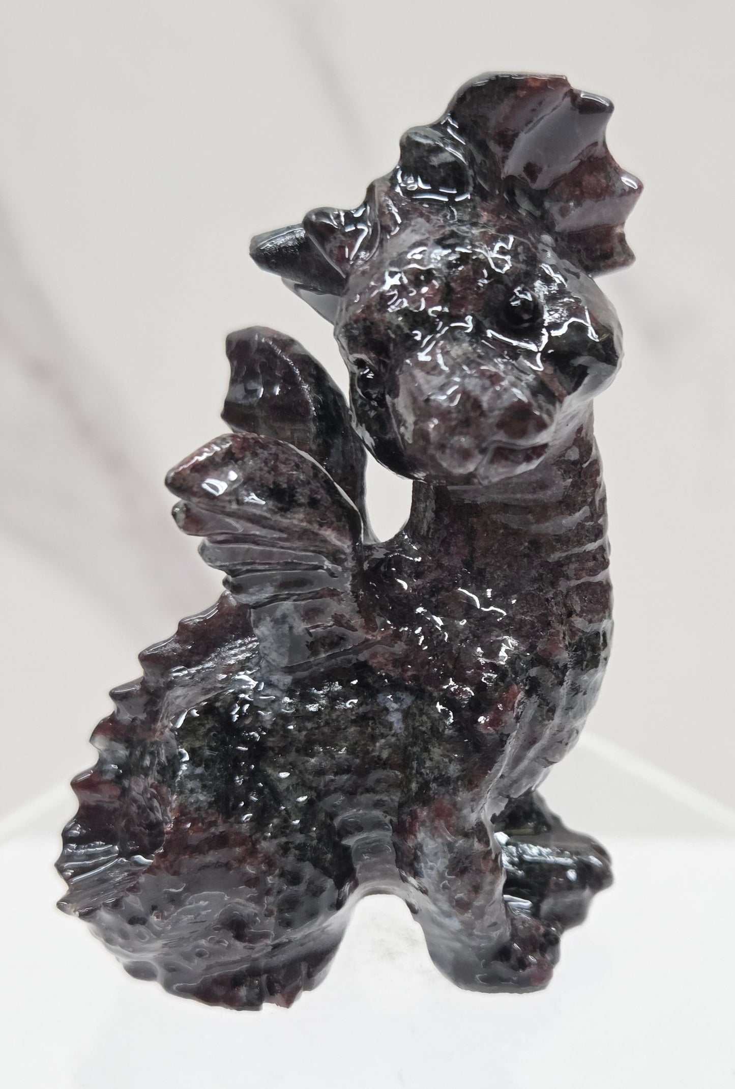Garnet crystal dragon carving on an acrylic stand against a neutral background