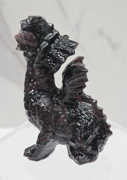 Garnet crystal dragon carving on an acrylic stand against a neutral background