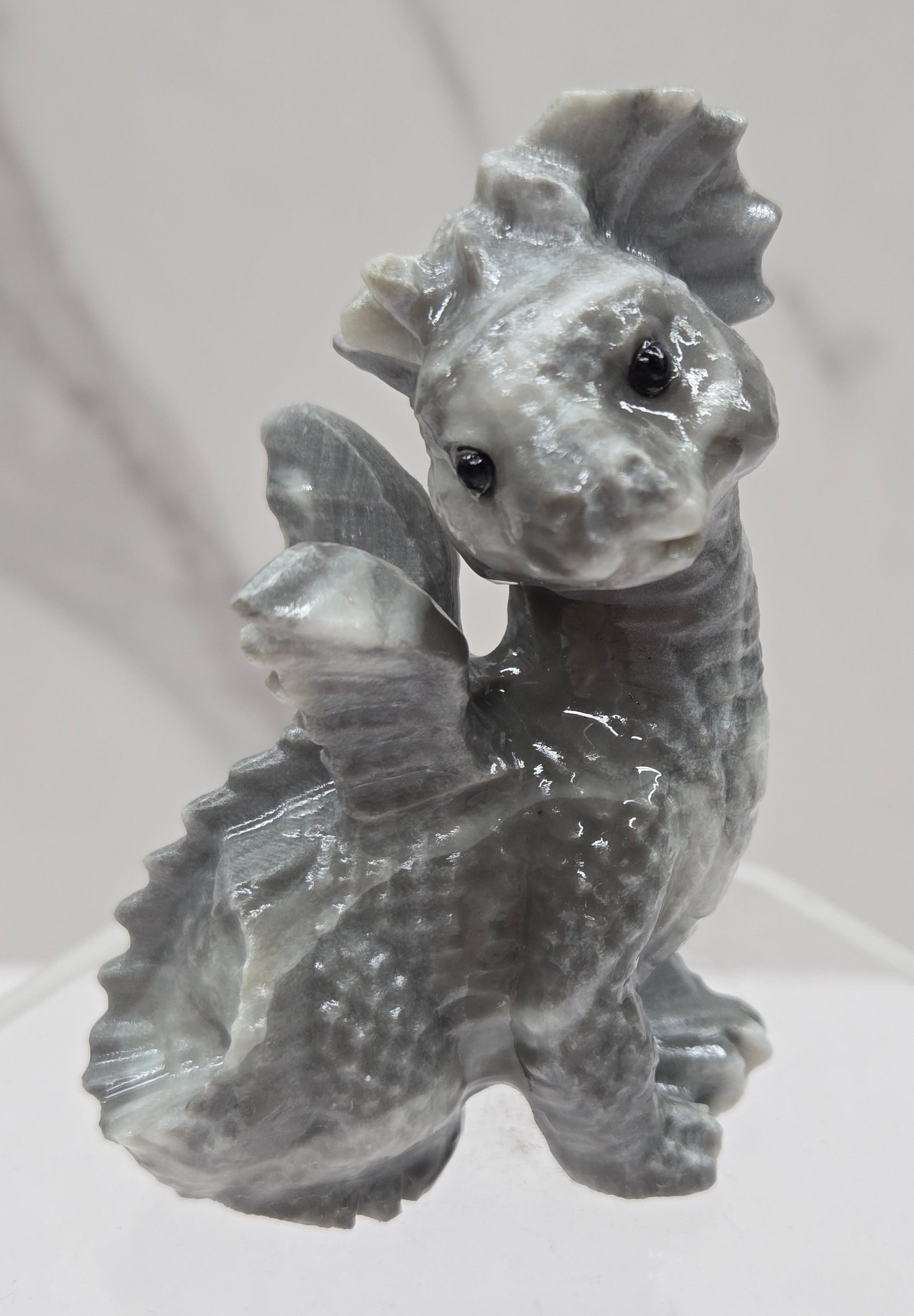 Grey and white crystal dragon carving on an acrylic stand against a neutral background