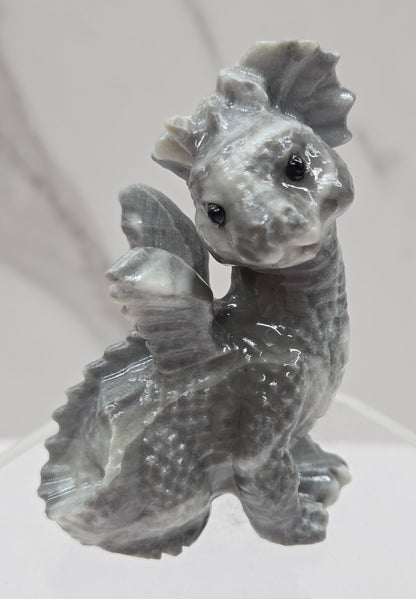 Grey and white crystal dragon carving on an acrylic stand against a neutral background