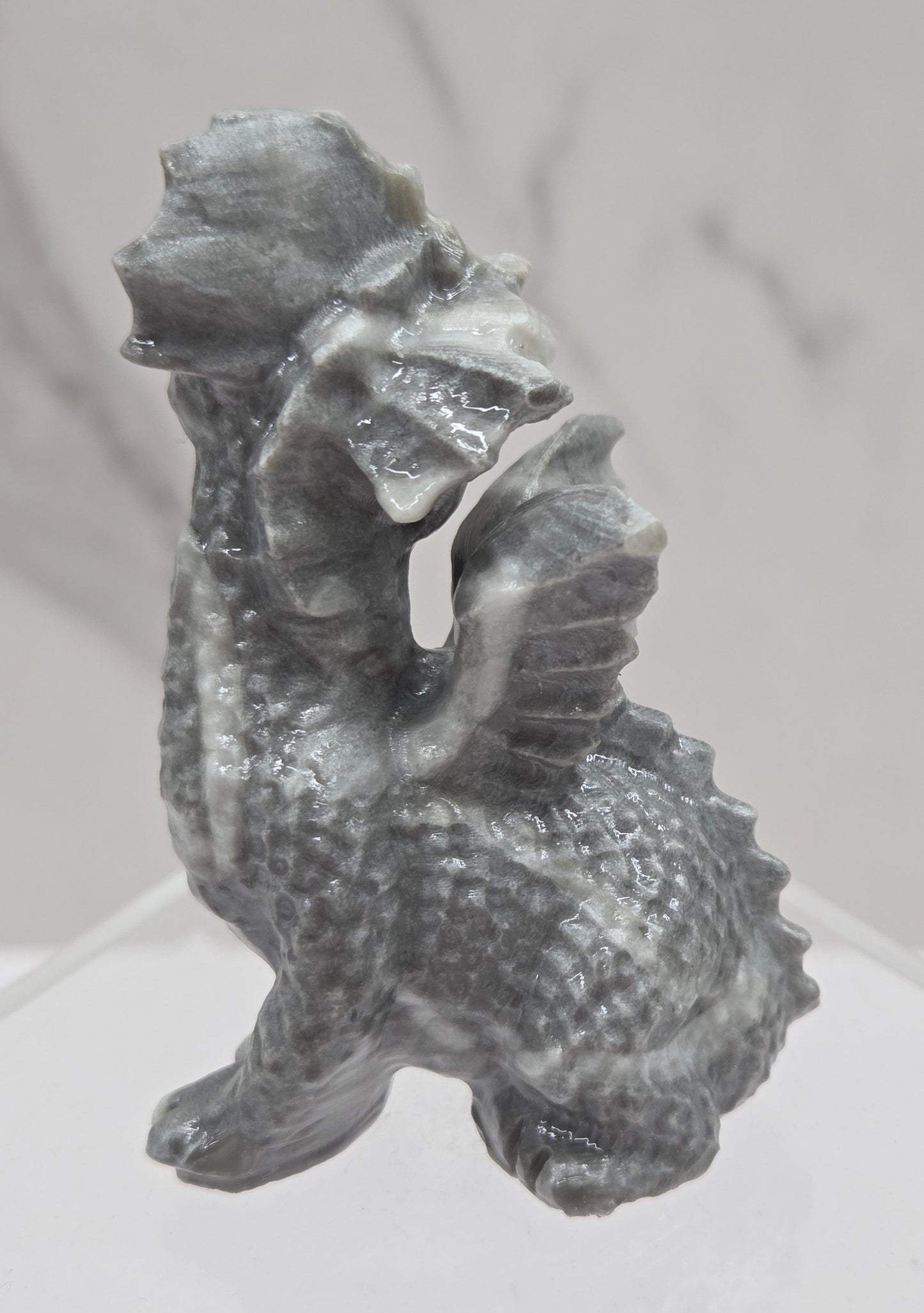 Grey and white crystal dragon carving on an acrylic stand against a neutral background