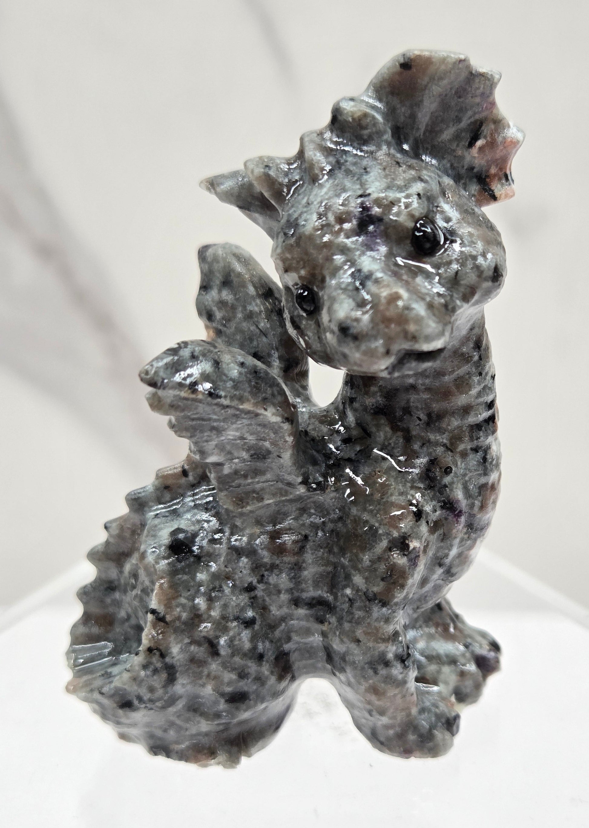 Yooperlite dragon carving on an acrylic stand against a neutral background