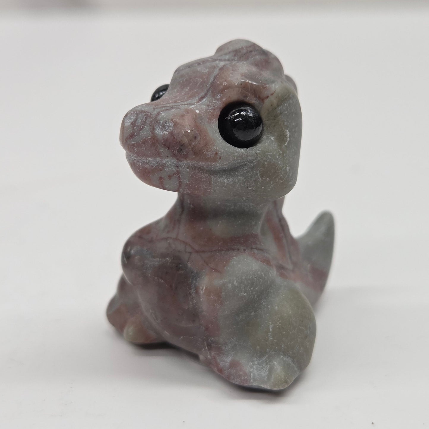 Small baby t-rex dinosaur carving made of Picture Jasper on a white surface