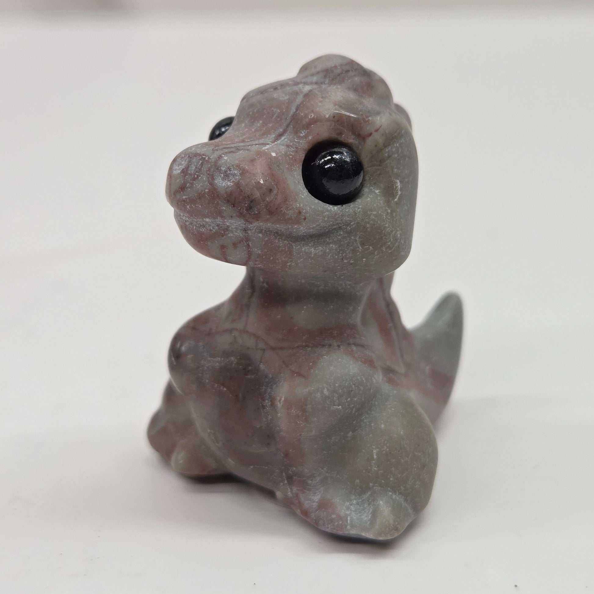 Small baby t-rex dinosaur carving made of Picture Jasper on a white surface