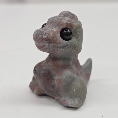 Small baby t-rex dinosaur carving made of Picture Jasper on a white surface