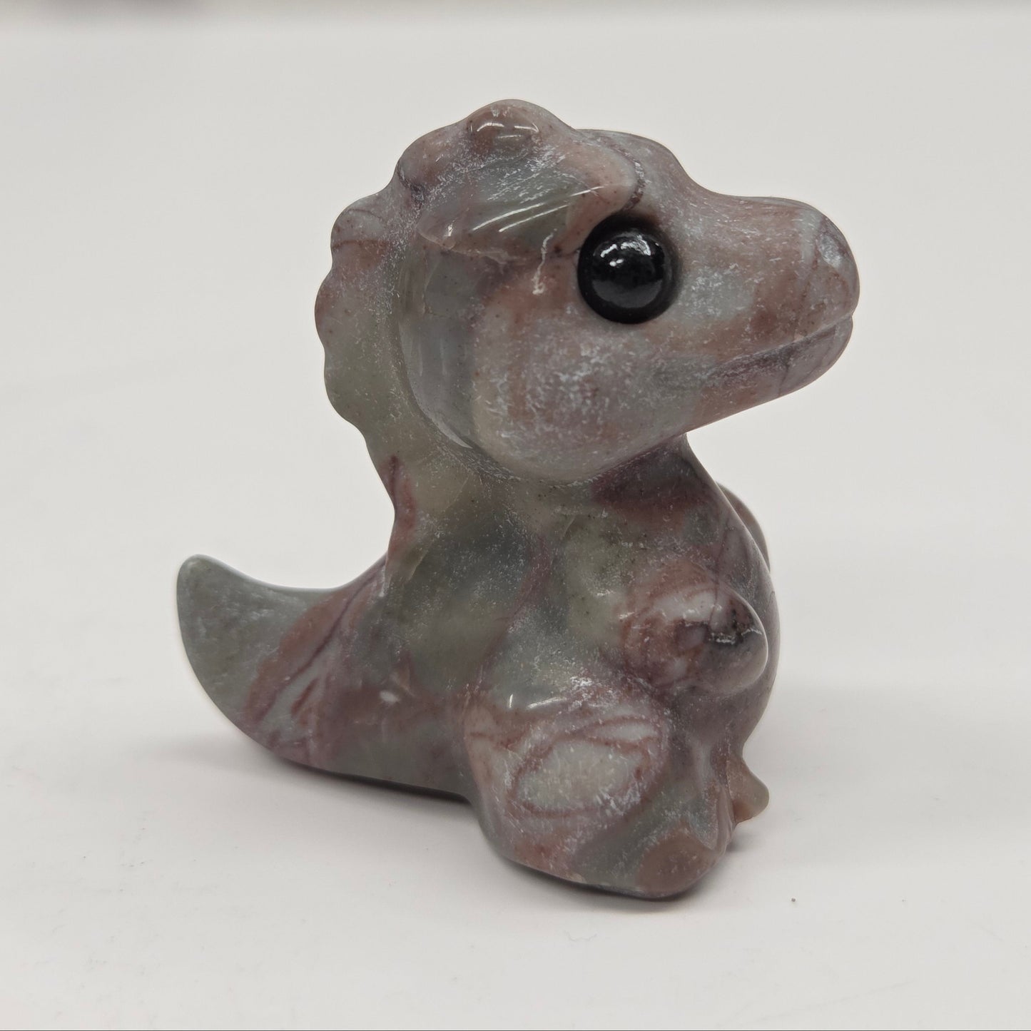 Small baby t-rex dinosaur carving made of Picture Jasper on a white surface