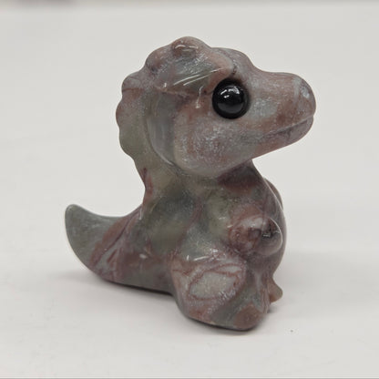 Small baby t-rex dinosaur carving made of Picture Jasper on a white surface