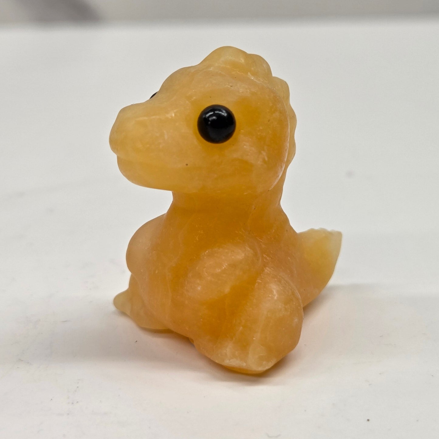 Small baby t-rex dinosaur carving made of Orange Calcite on a white surface