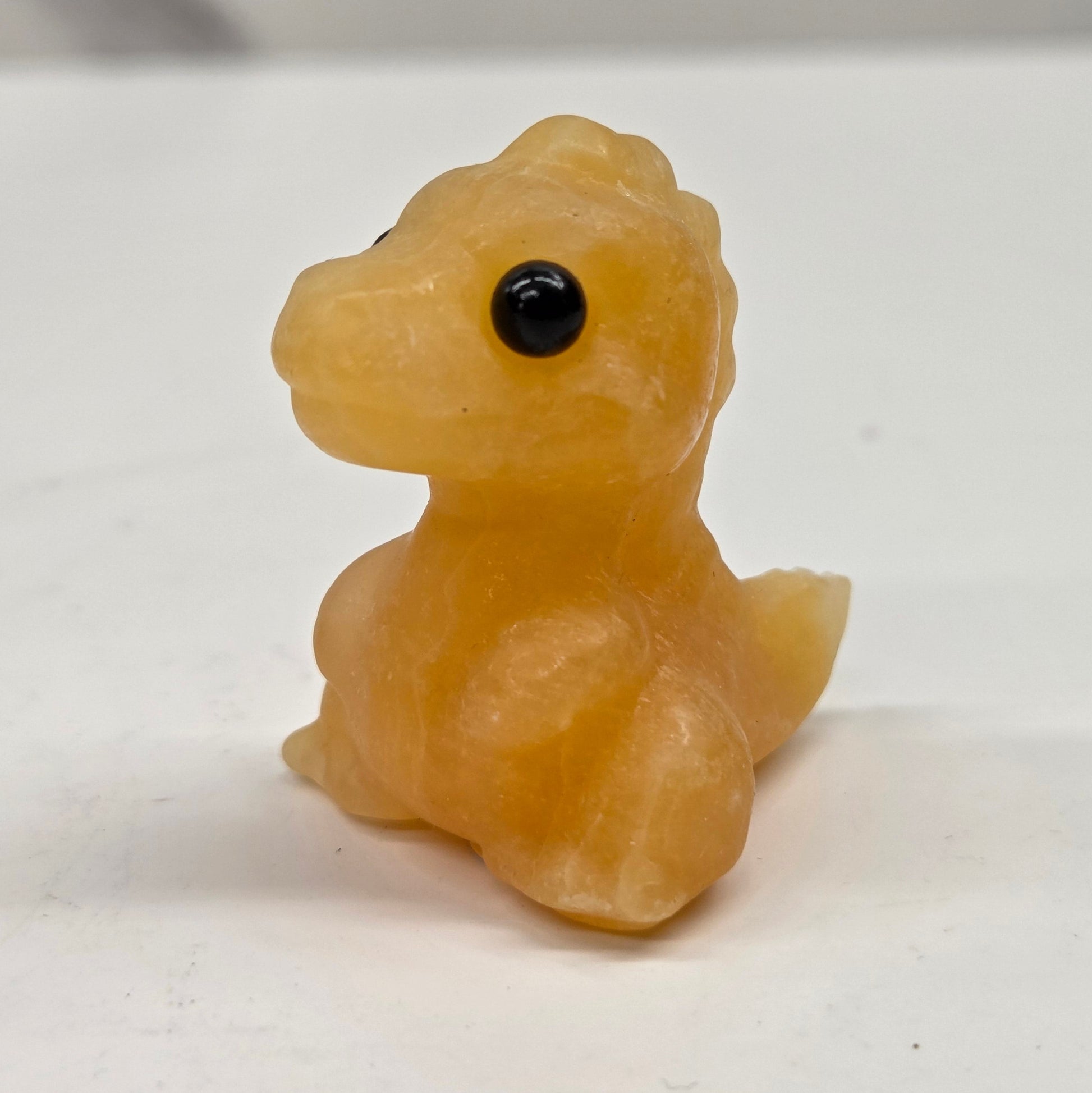 Small baby t-rex dinosaur carving made of Orange Calcite on a white surface