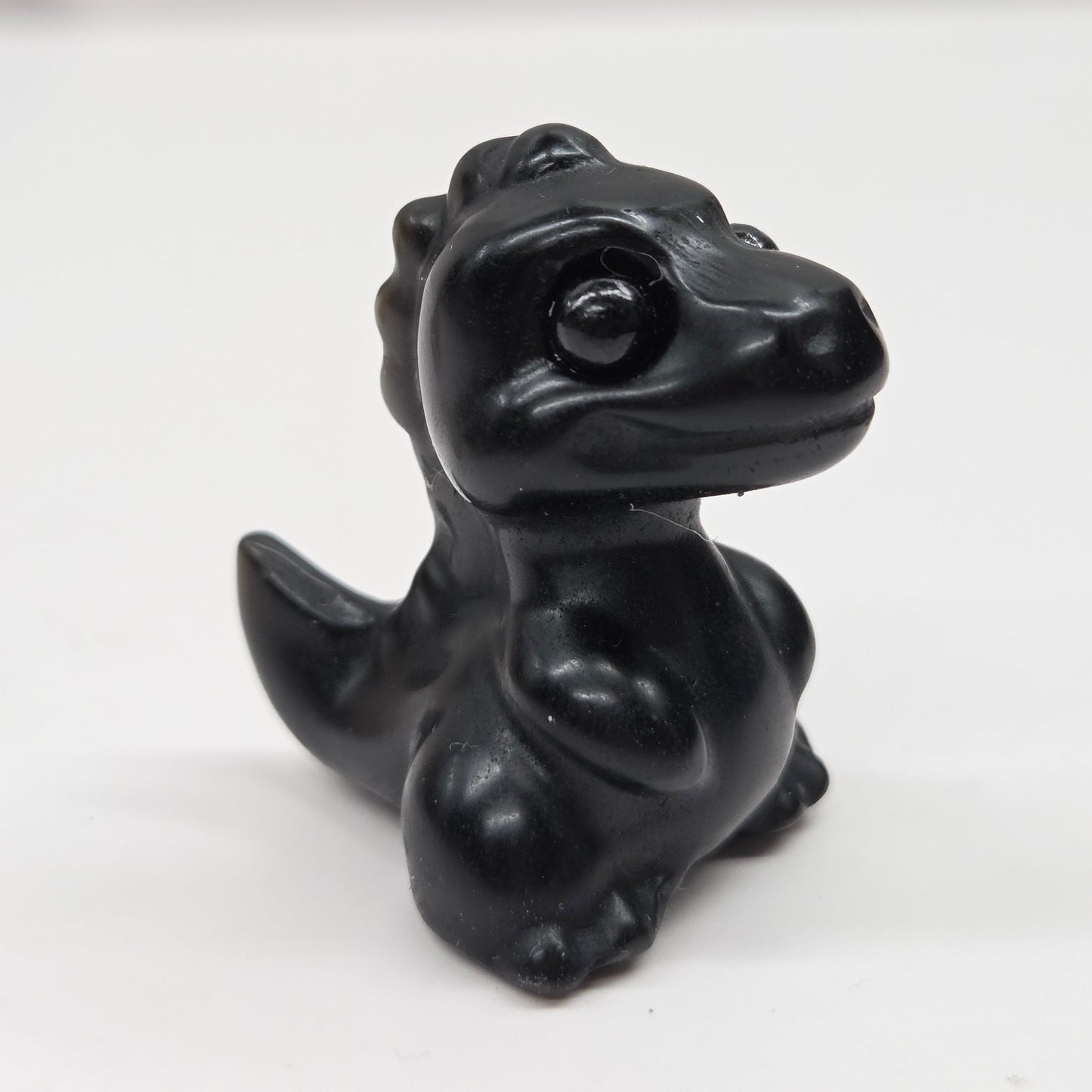 Small baby t-rex dinosaur carving made of Obsidian on a white surface