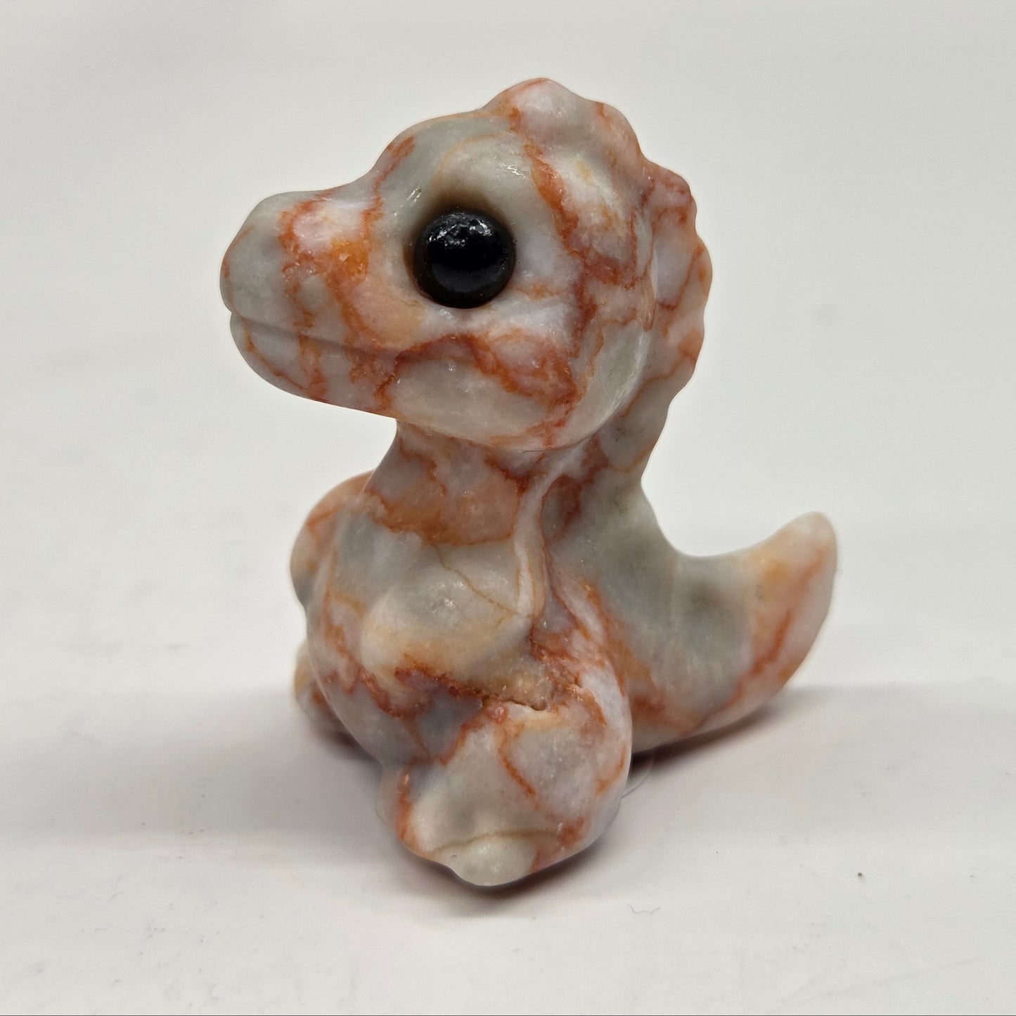 Small baby t-rex dinosaur carving made of Red Vein Jasper on a white surface