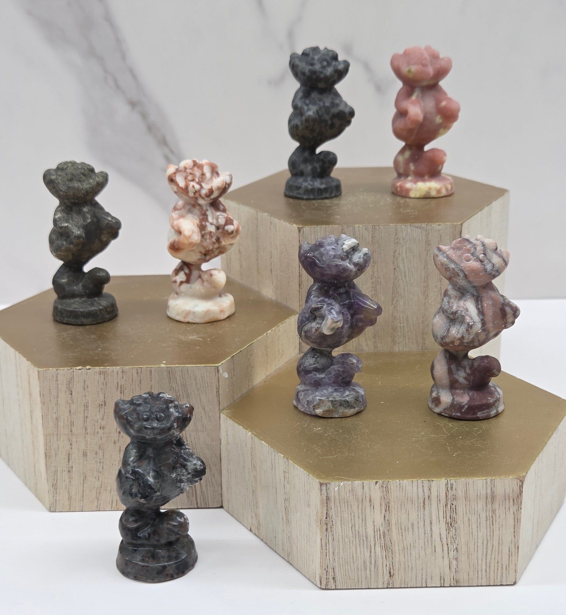 Cheshire Cat carvings in a variety of materials and colors on a wooden stand against a neutral background