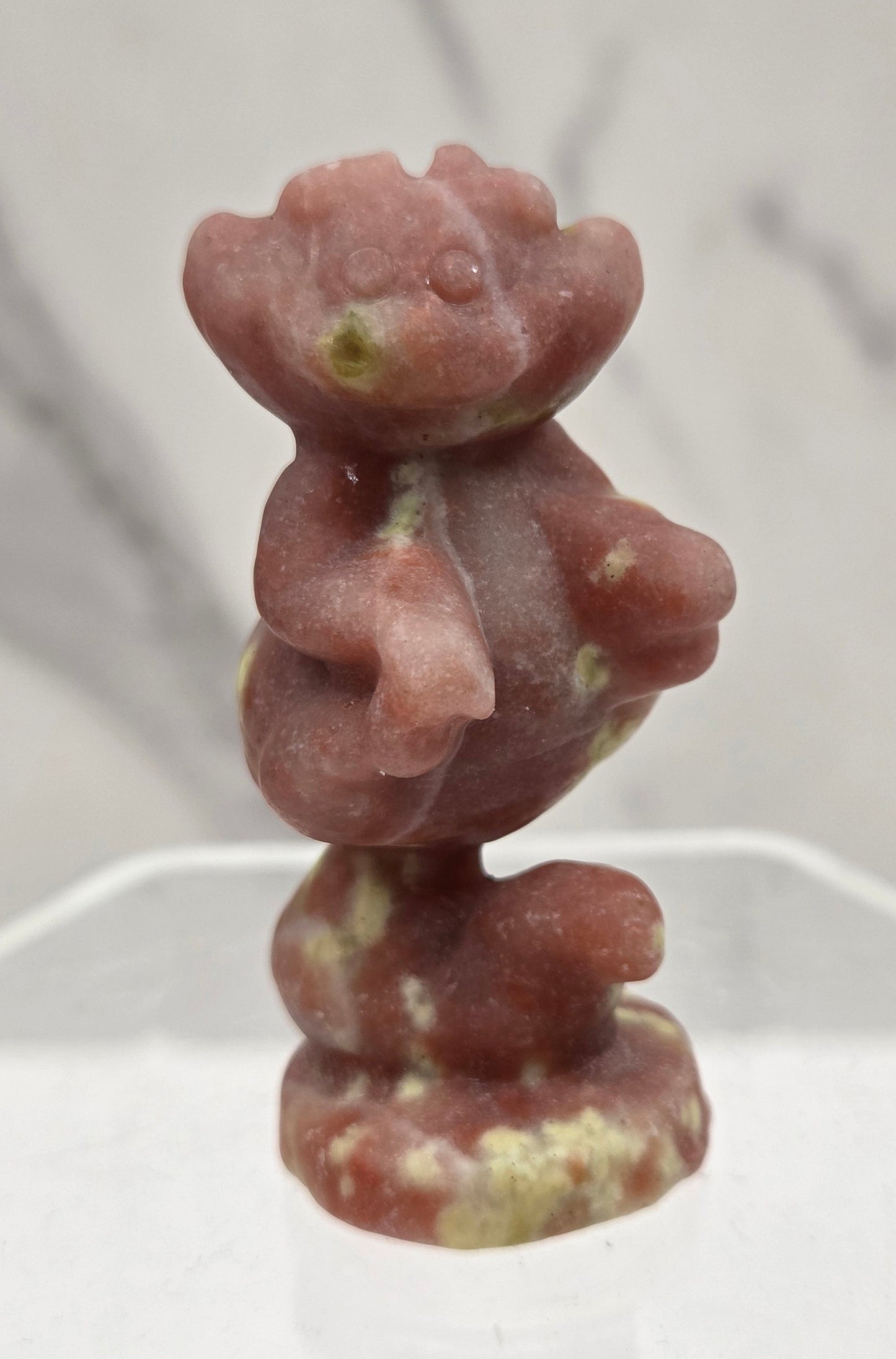 Cheshire Cat carving made of Red Serpentine on a clear stand against a neutral background