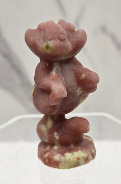 Cheshire Cat carving made of Red Serpentine on a clear stand against a neutral background
