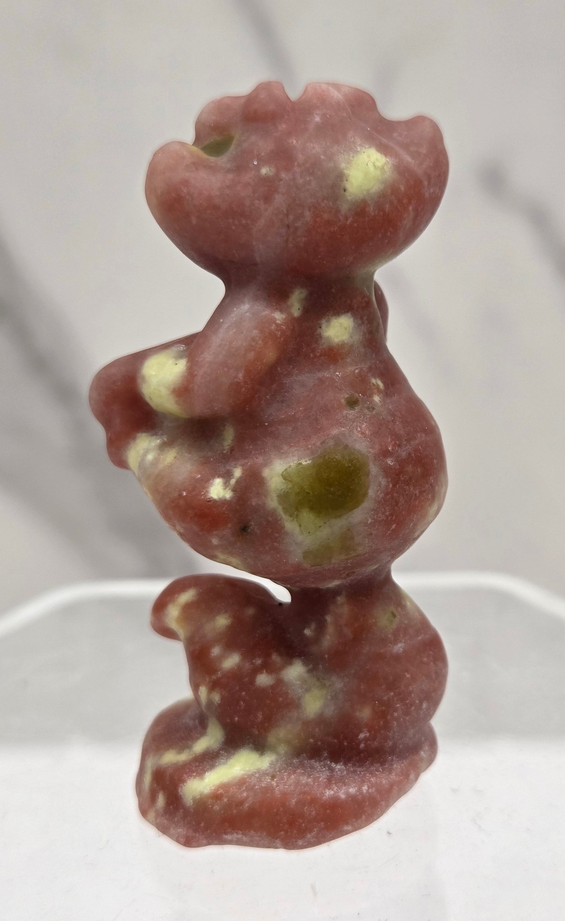 Cheshire Cat carving made of Red Serpentine on a clear stand against a neutral background