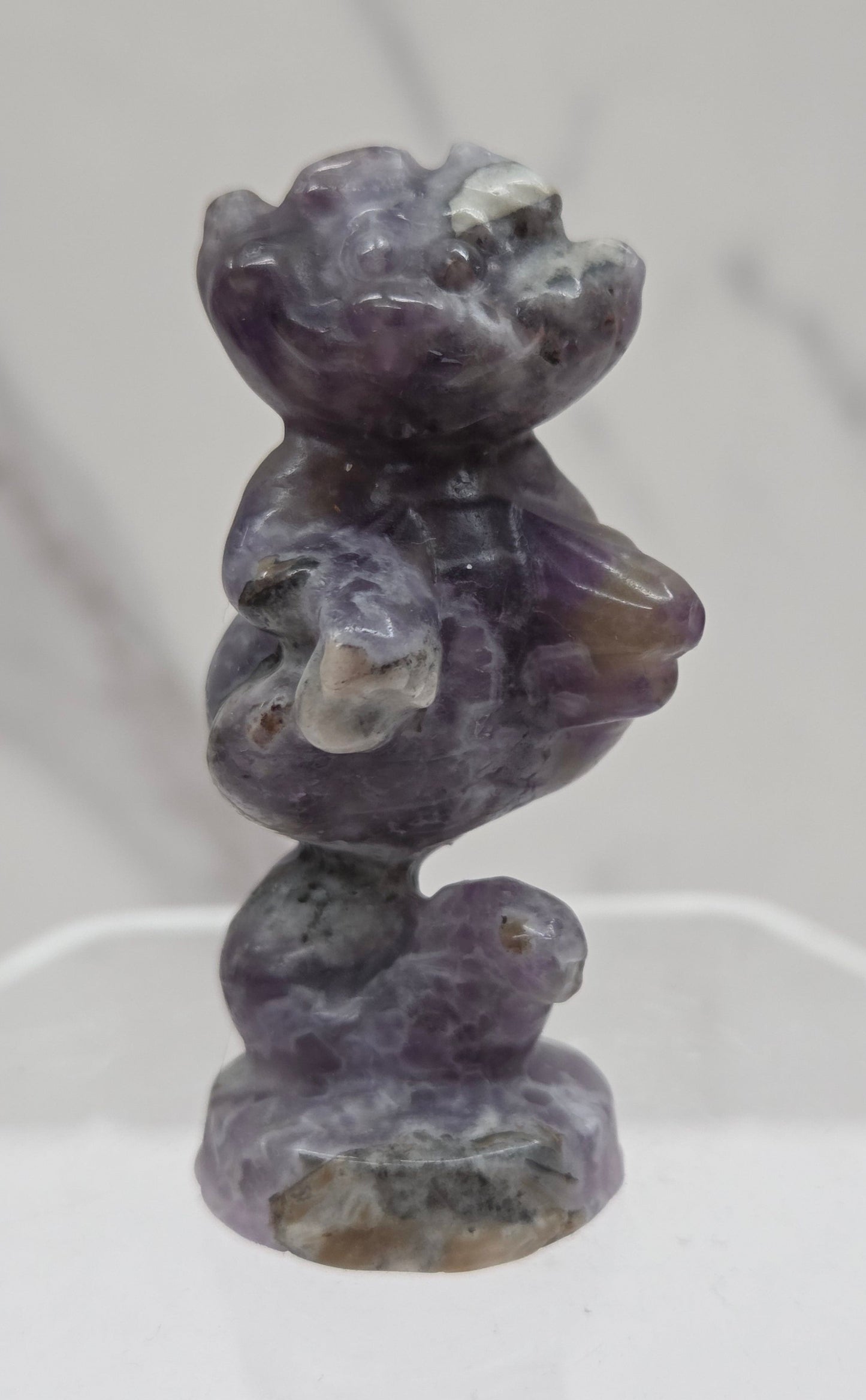 Cheshire Cat carving made of Fluorite Root on a clear stand against a neutral background