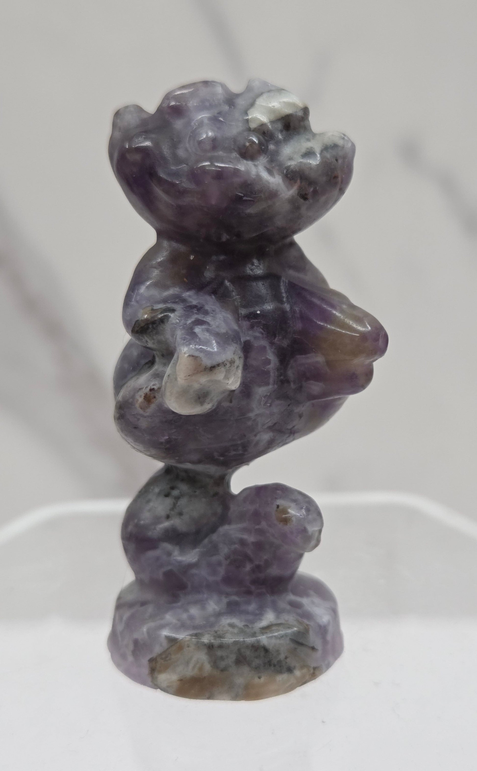 Cheshire Cat carving made of Fluorite Root on a clear stand against a neutral background