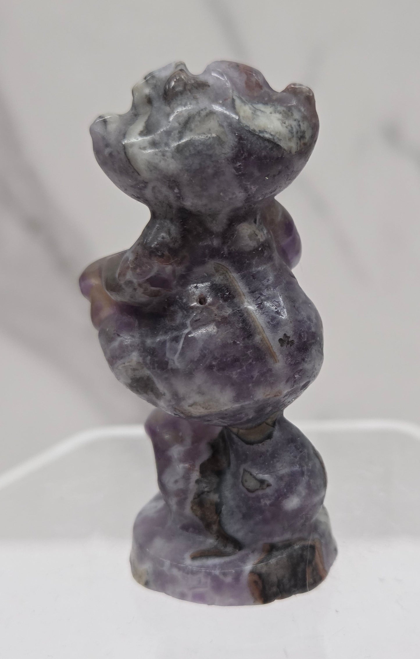 Cheshire Cat carving made of Fluorite Root on a clear stand against a neutral background