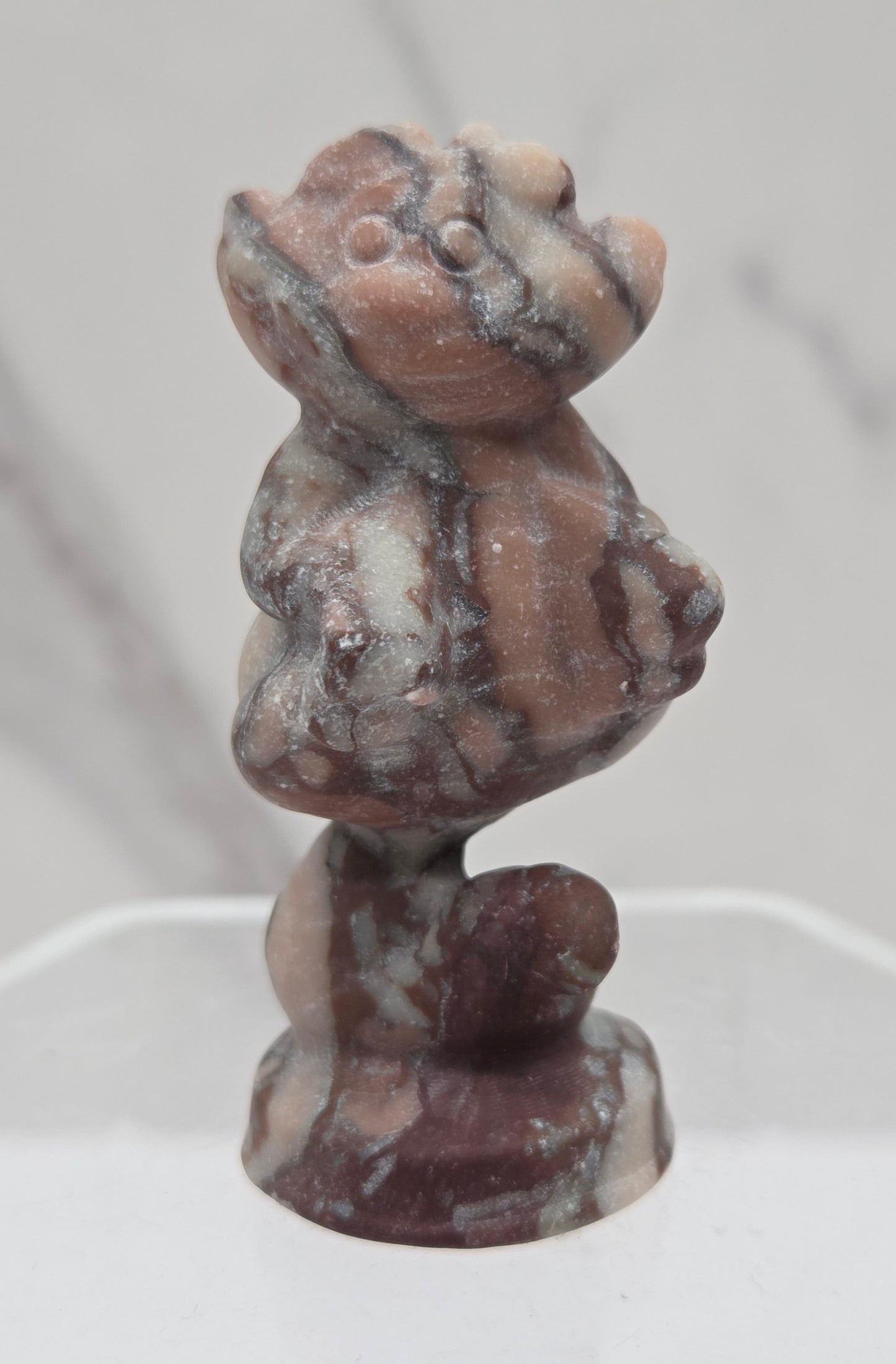 Cheshire Cat carving made of Chocolate Jasper on a clear stand against a neutral background