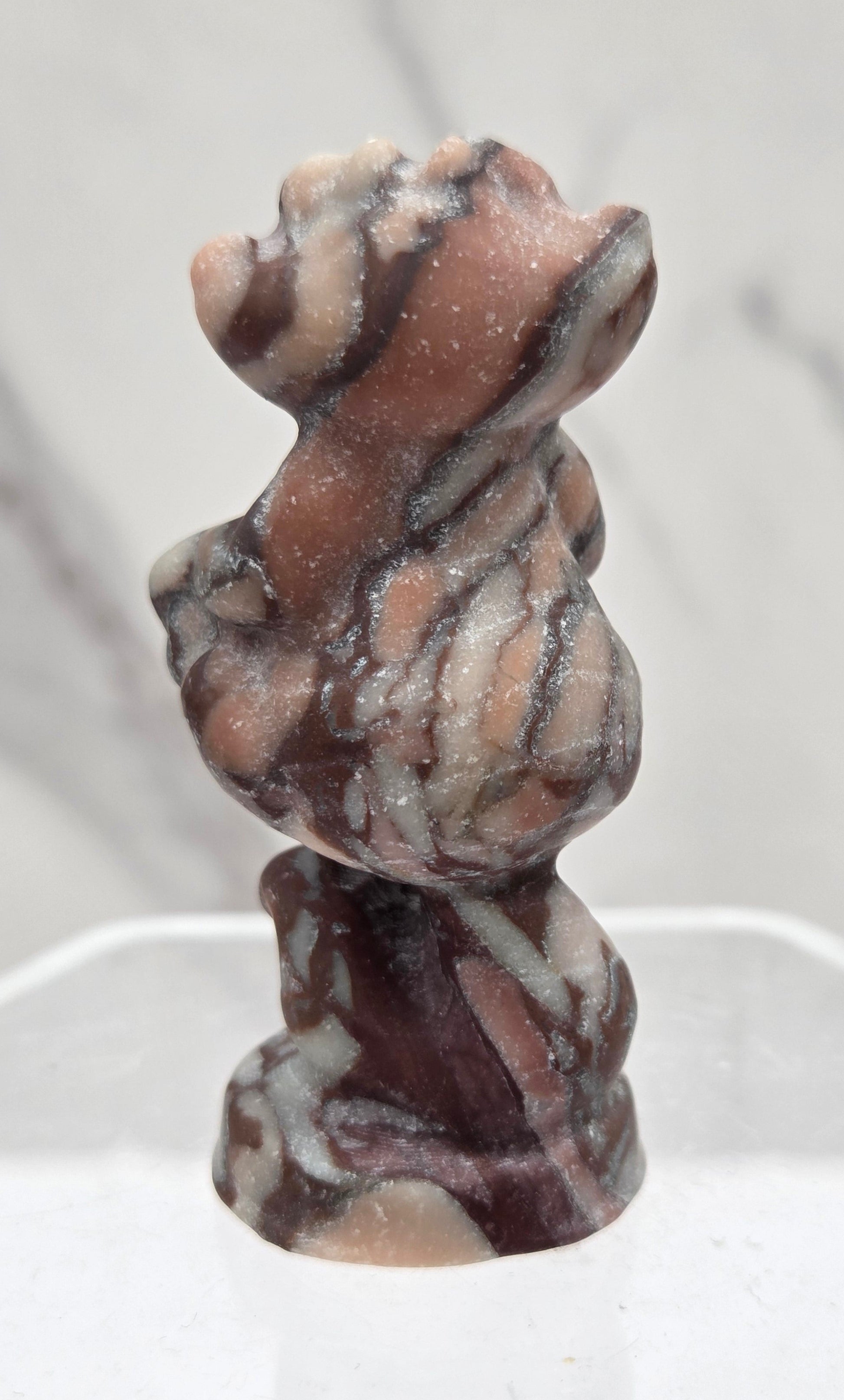 Cheshire Cat carving made of Chocolate Jasper on a clear stand against a neutral background