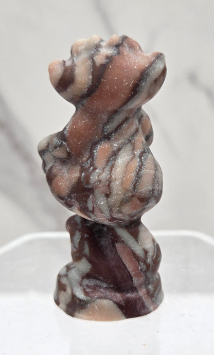 Cheshire Cat carving made of Chocolate Jasper on a clear stand against a neutral background