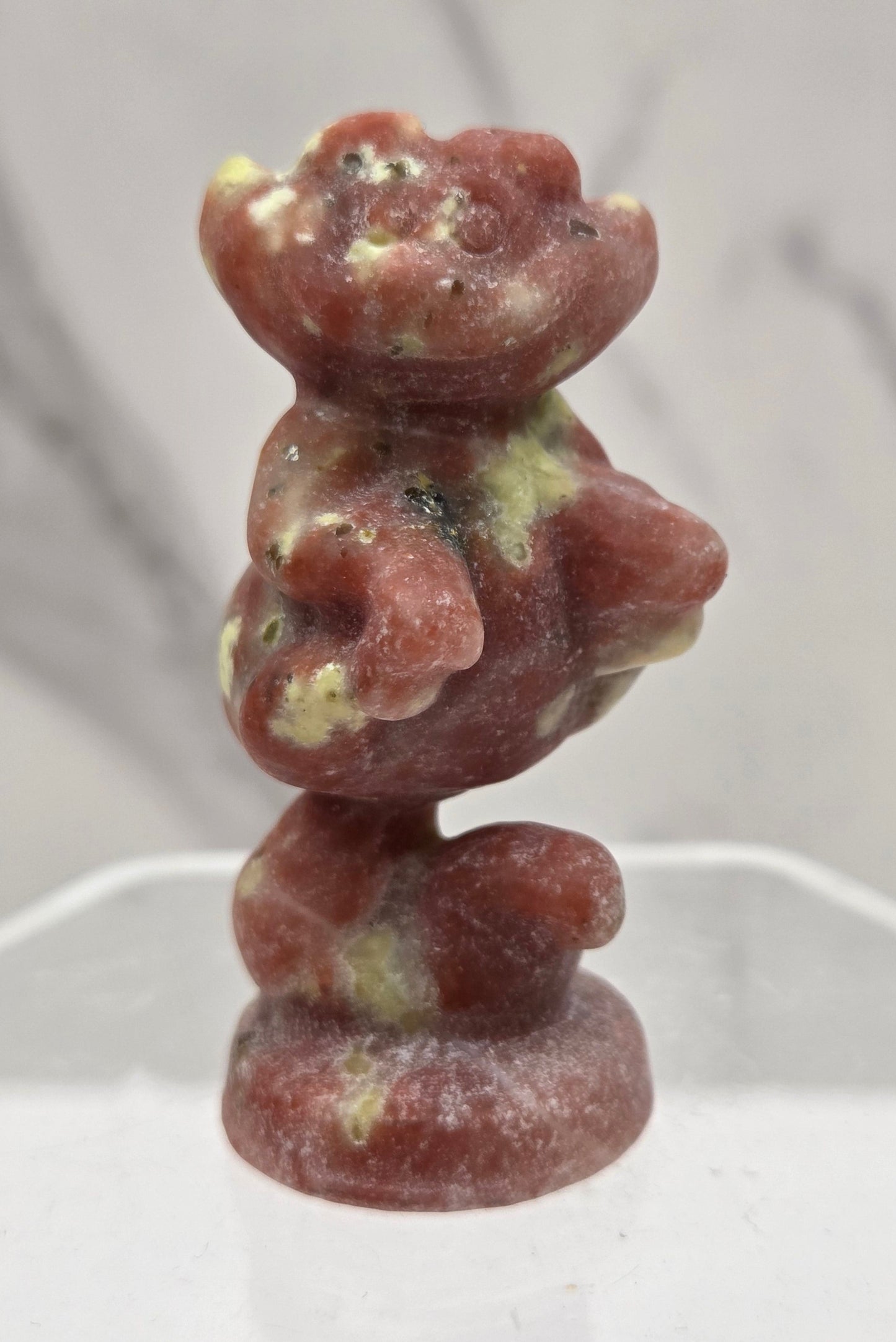 Cheshire Cat carving made of Red Serpentine on a clear stand against a neutral background
