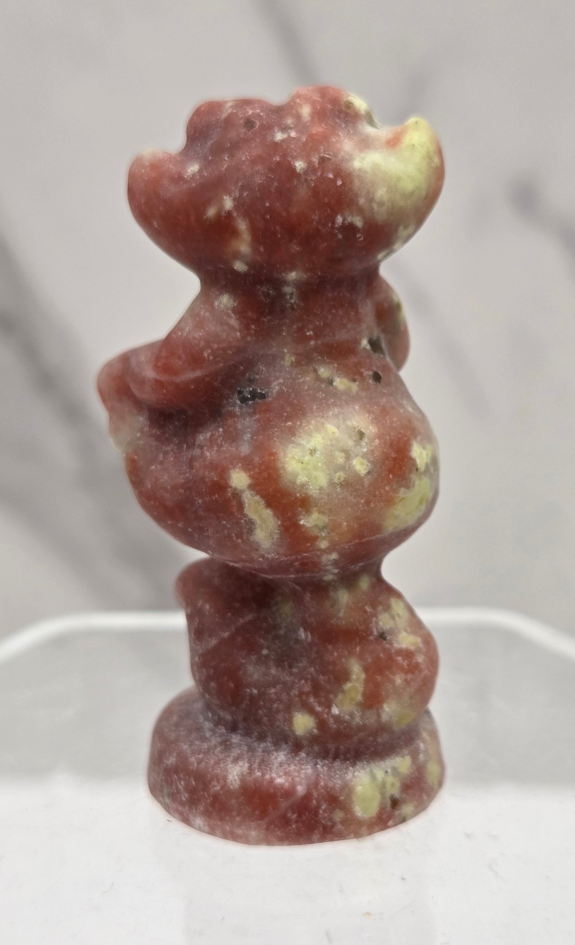 Cheshire Cat carving made of Red Serpentine on a clear stand against a neutral background