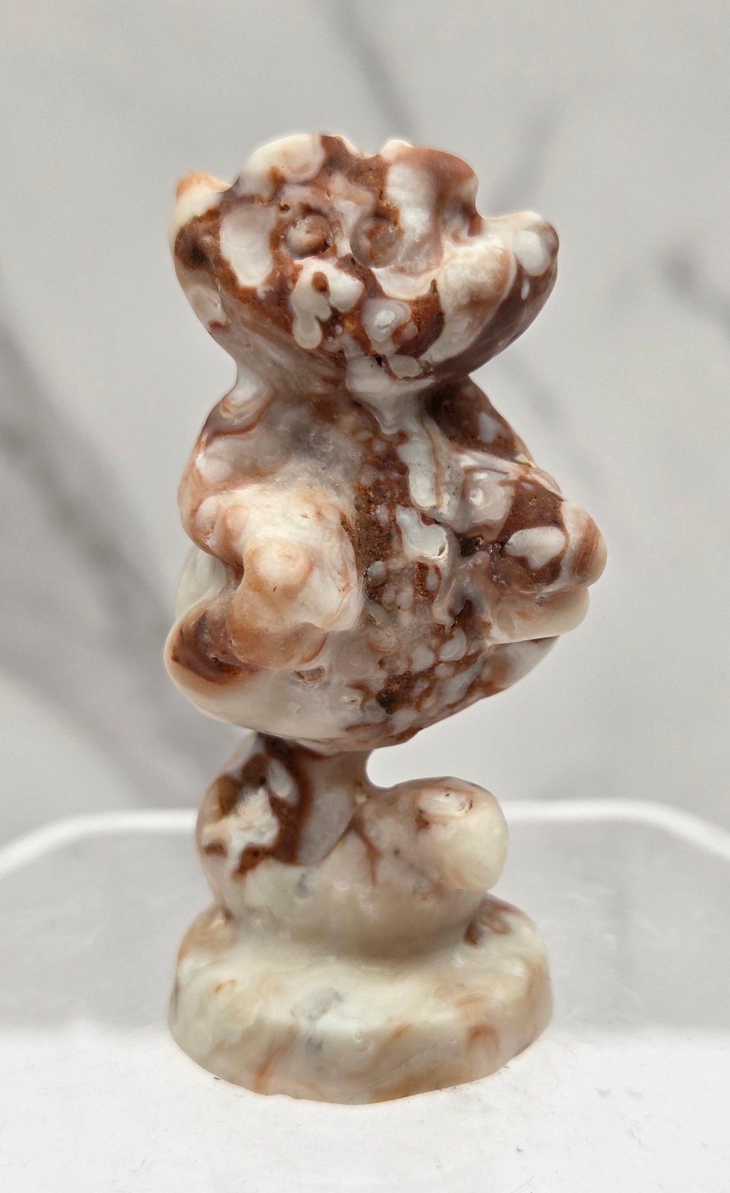 Cheshire Cat carving made of Amber Calcite on a clear stand against a neutral background