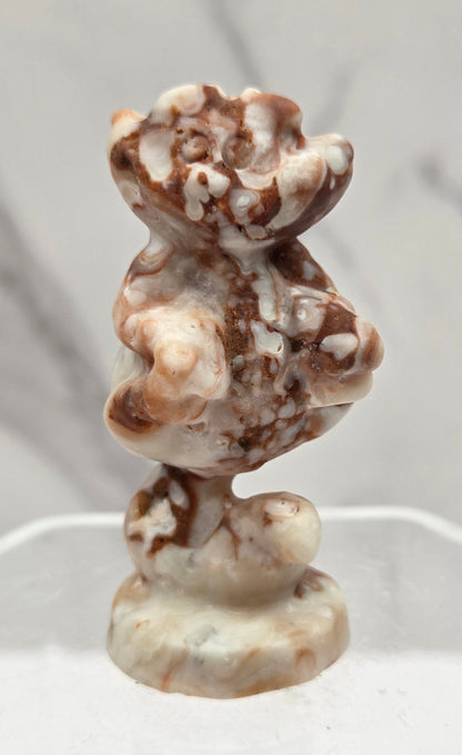 Cheshire Cat carving made of Amber Calcite on a clear stand against a neutral background