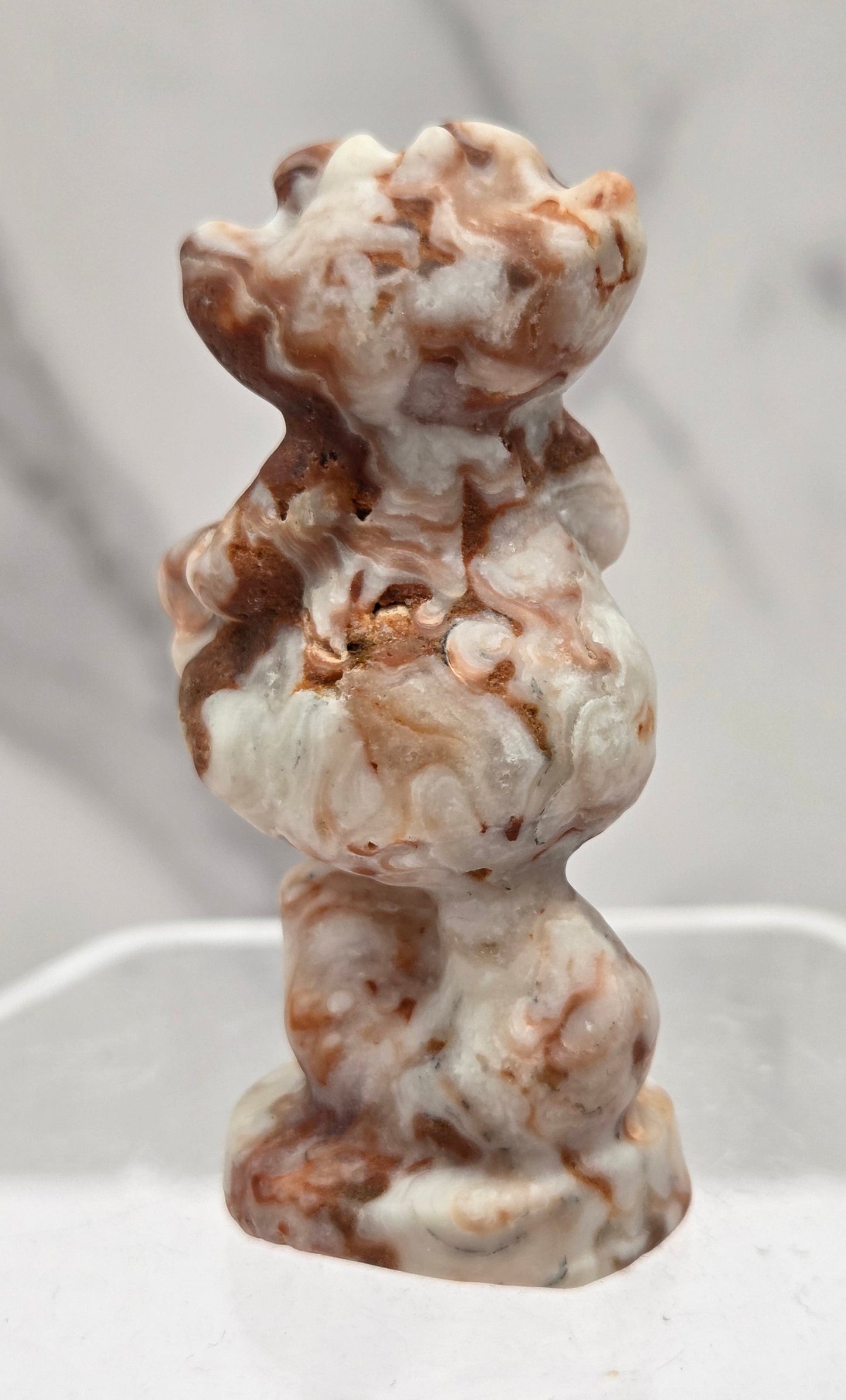 Cheshire Cat carving made of Amber Calcite on a clear stand against a neutral background