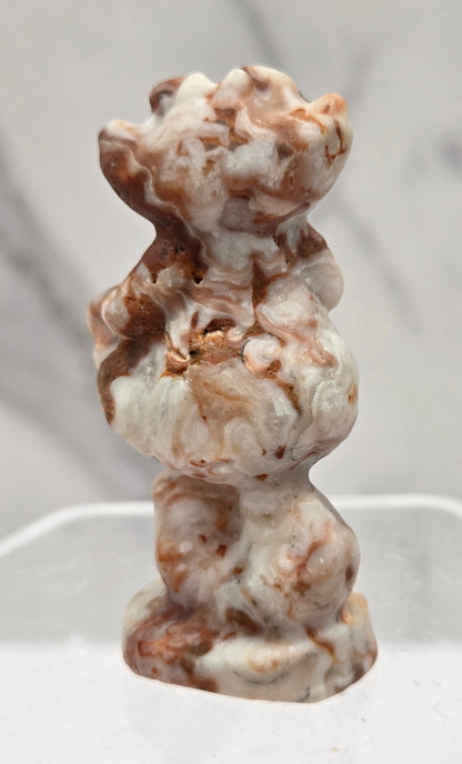 Cheshire Cat carving made of Amber Calcite on a clear stand against a neutral background