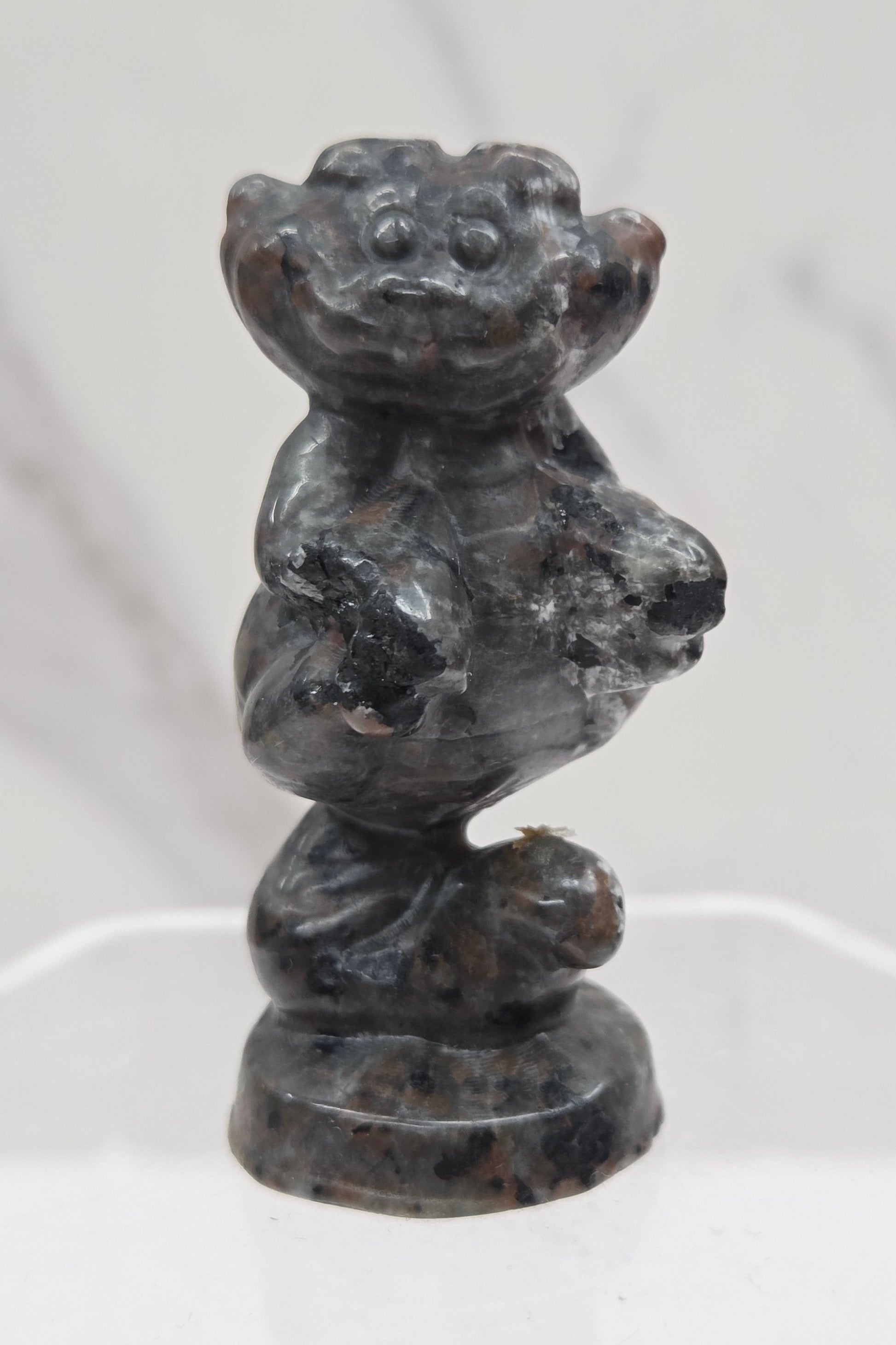 Cheshire Cat carving made of Yooperlite on a clear stand against a neutral background