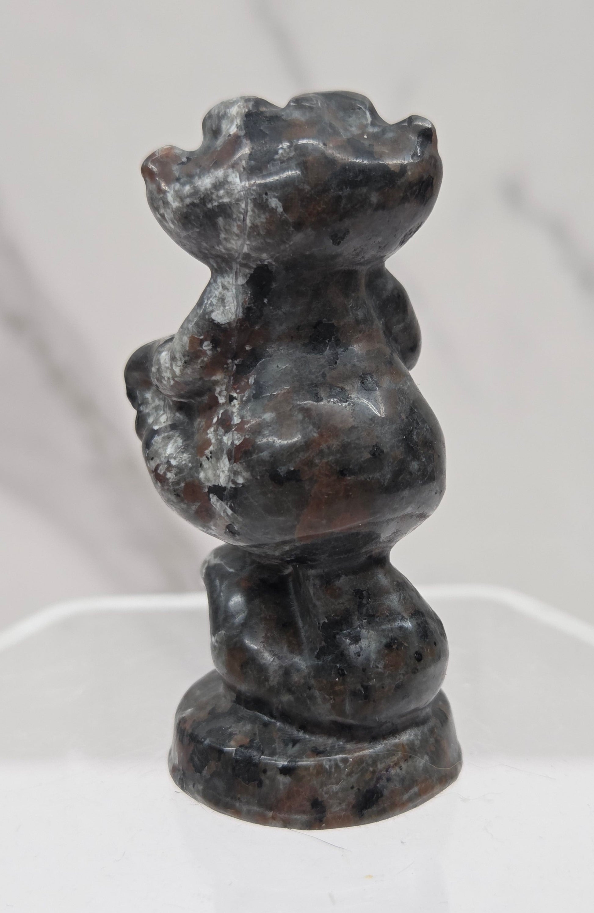 Cheshire Cat carving made of Yooperlite on a clear stand against a neutral background