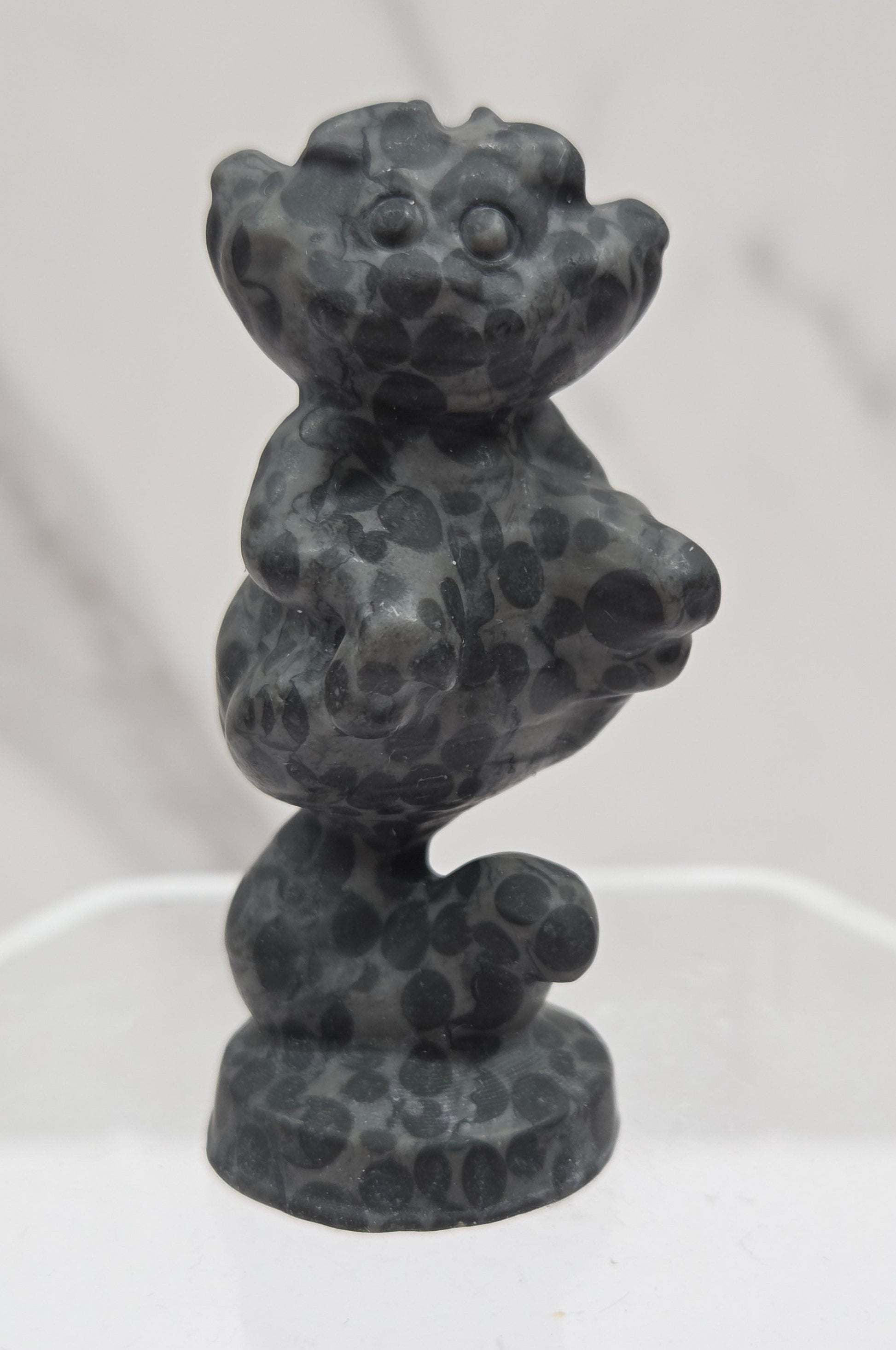 Cheshire Cat carving made of Leopard Jasper on a clear stand against a neutral background