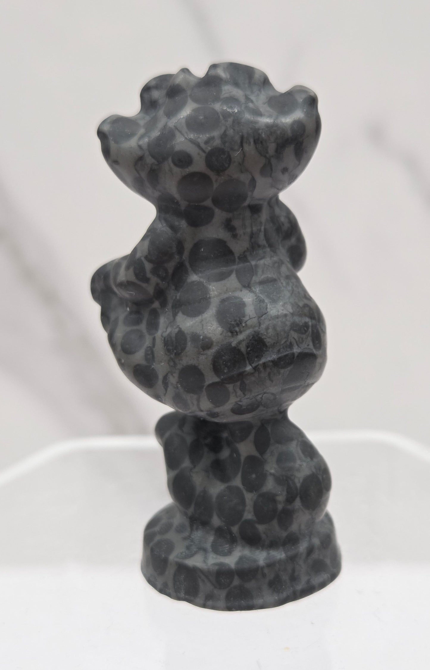 Cheshire Cat carving made of Leopard Jasper on a clear stand against a neutral background