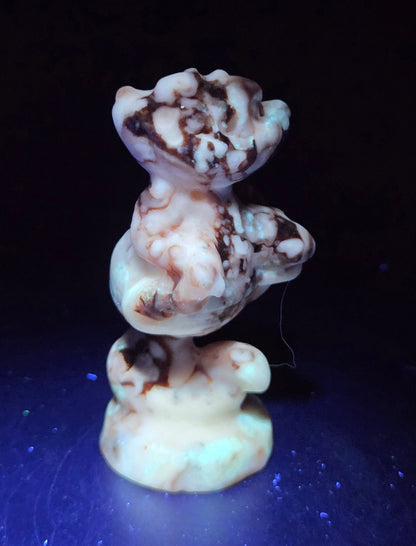 Cheshire Cat carving made of Amber Calcite against a neutral background under UV light