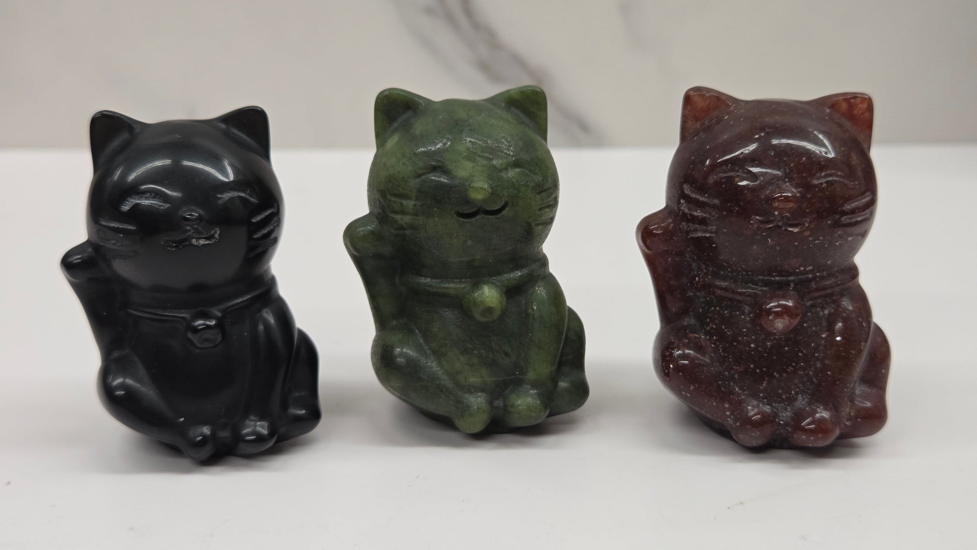 Three cat-shaped figurines in black, green, and brown on a white background