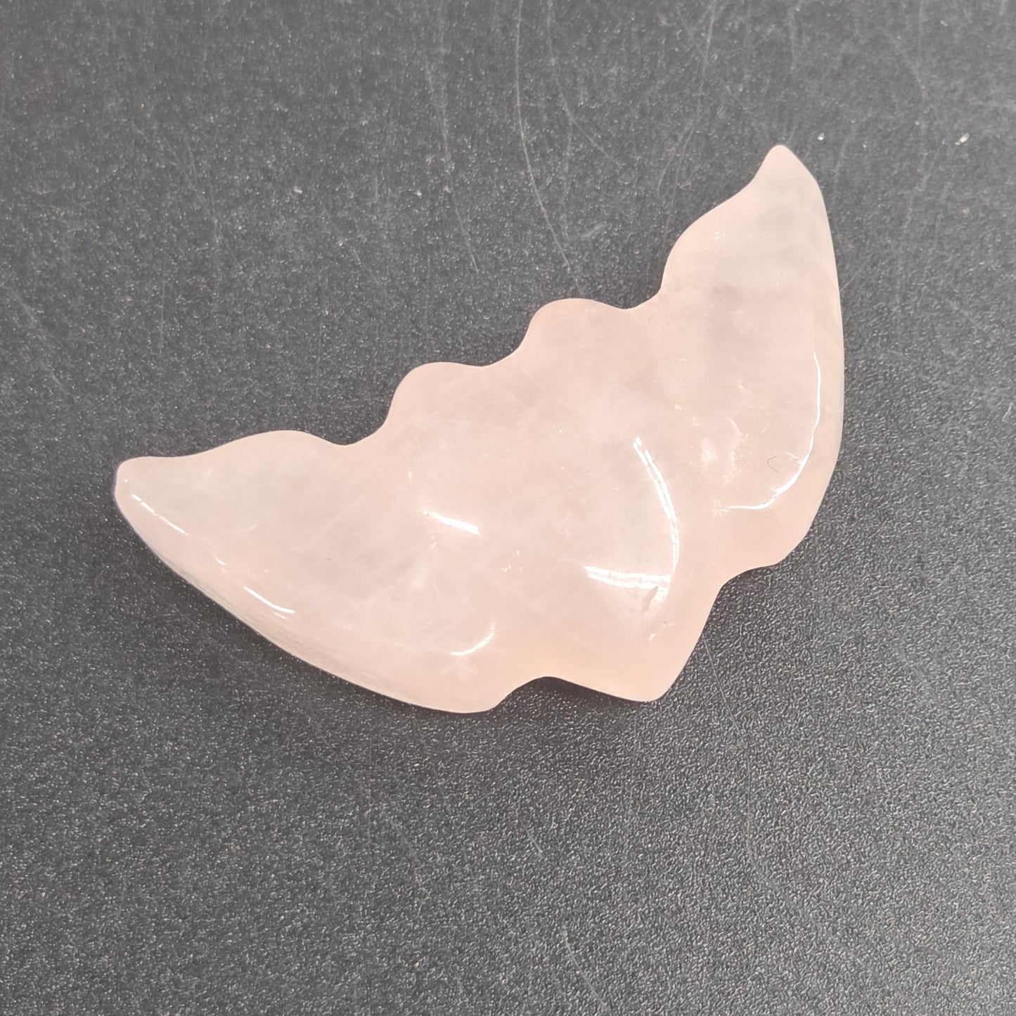 Rose Quartz stone heart with wing carvings on a black background
