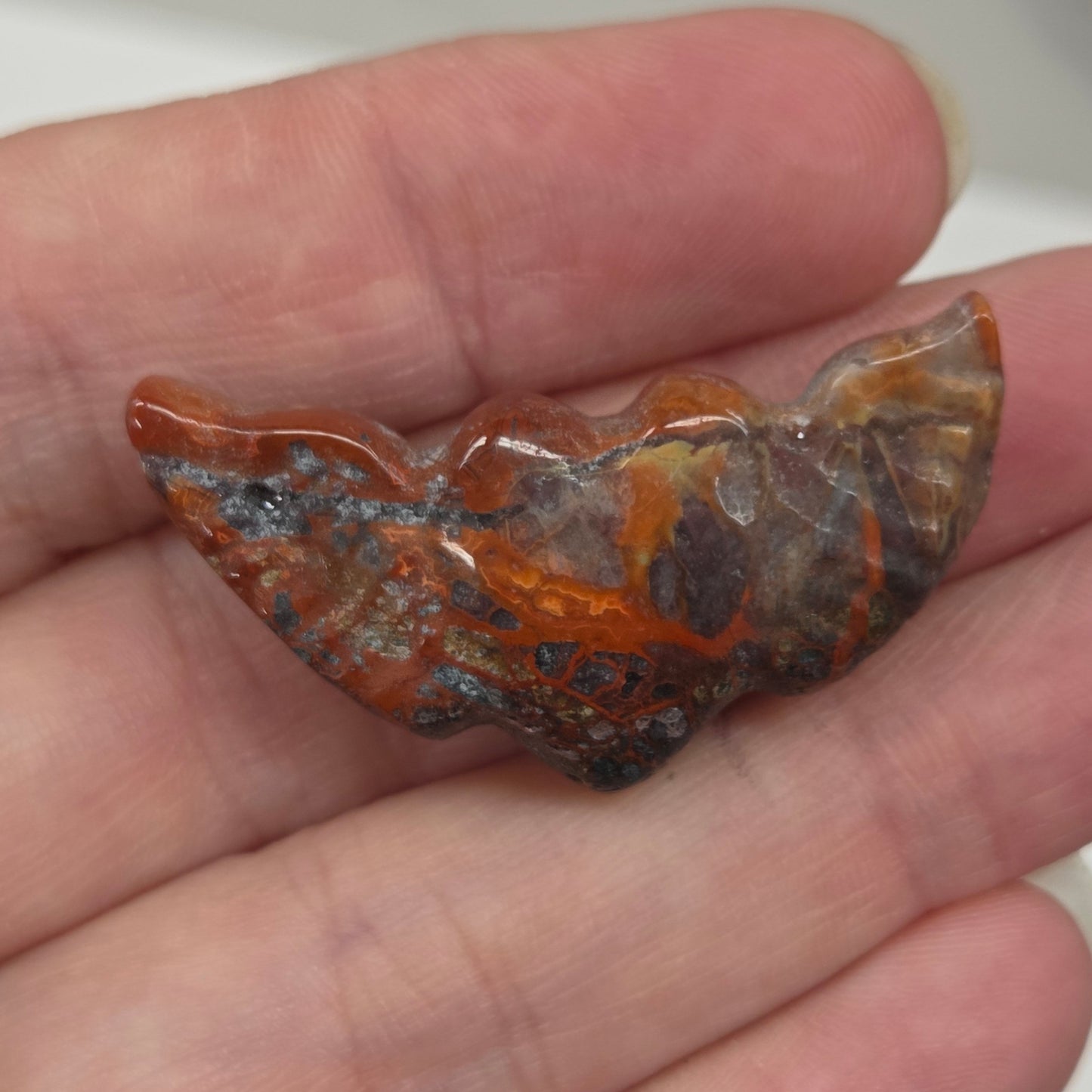 Hand holding a Crazy Lace Agate stone heart with wing carvings on a white background