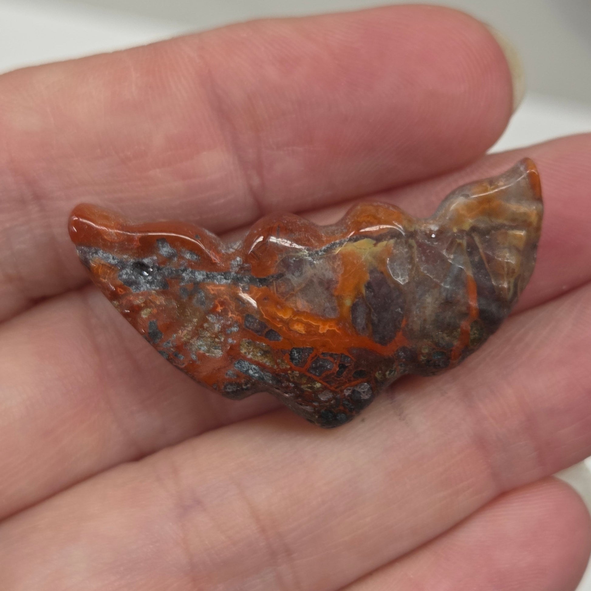 Hand holding a Crazy Lace Agate stone heart with wing carvings on a white background