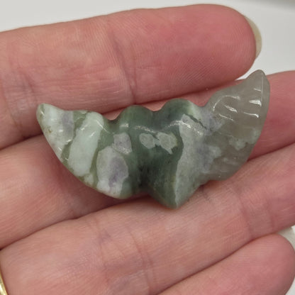 Hand holding a Green Jade stone heart with wing carvings on a white background
