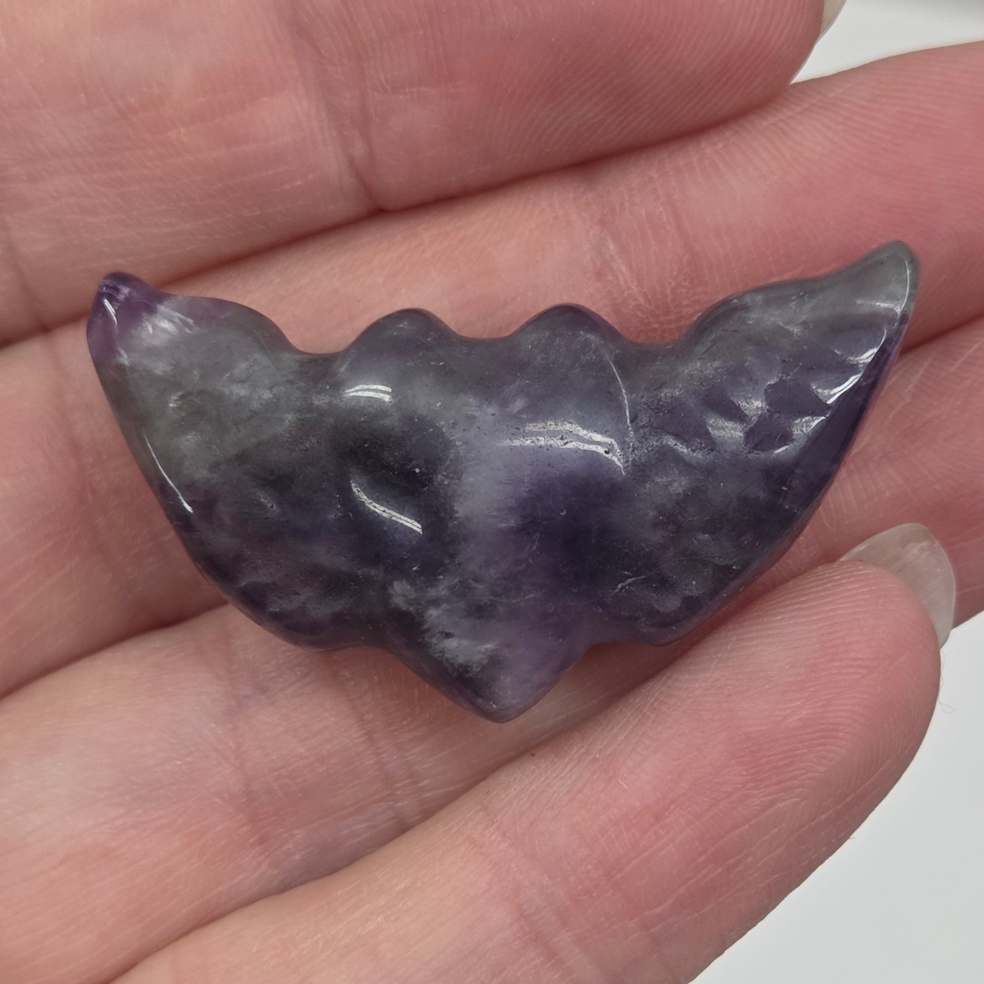 Hand holding a Amethyst stone heart with wing carvings on a white background