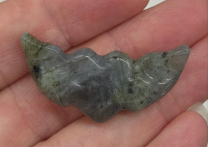 Hand holding a Labradorite stone heart with wing carvings on a white background