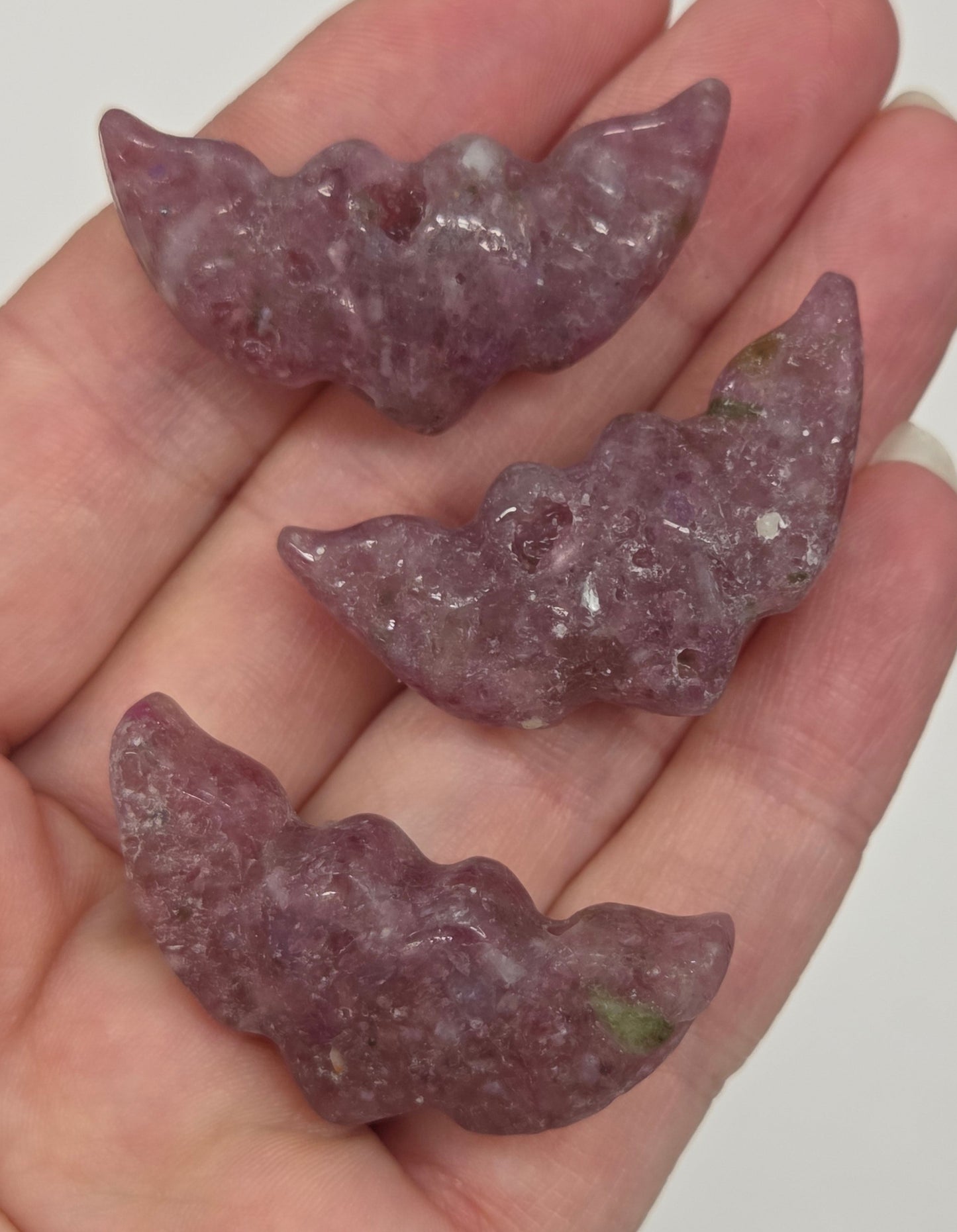 Hand holding Pink Tourmaline stone heart with wing carvings on a white background