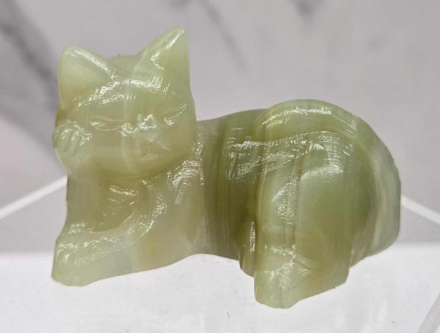 Afghan Jade cat carving lying down on an acrylic stand against a neutral background