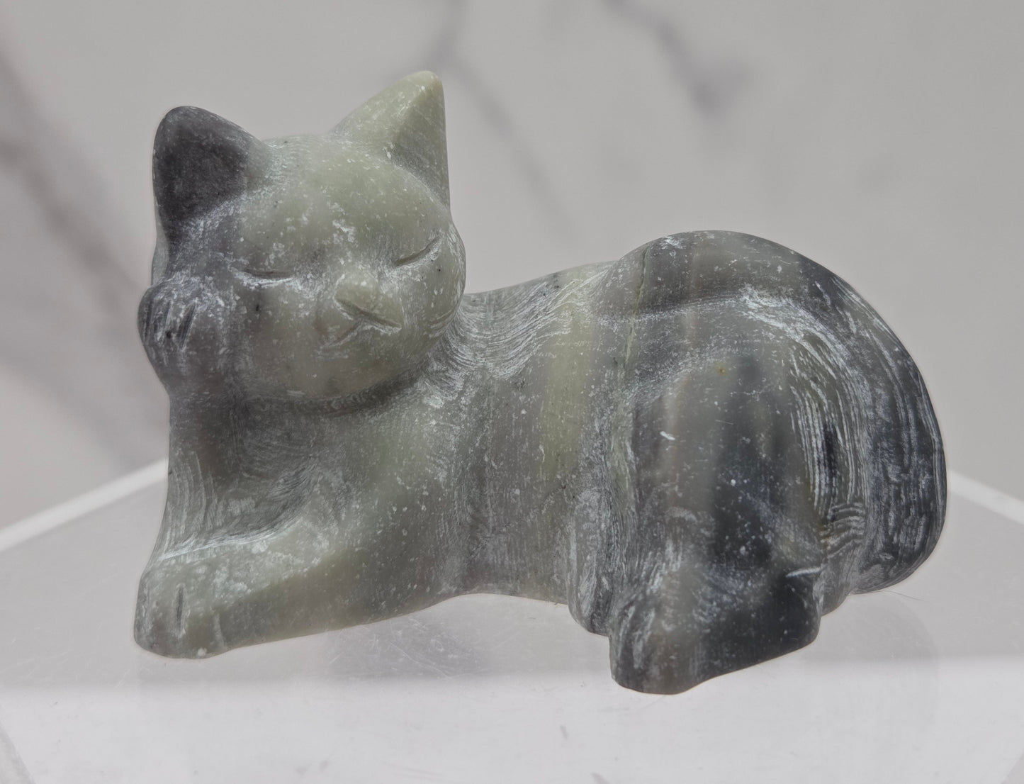 Jasper cat carving lying down an acrylic stand against a neutral background