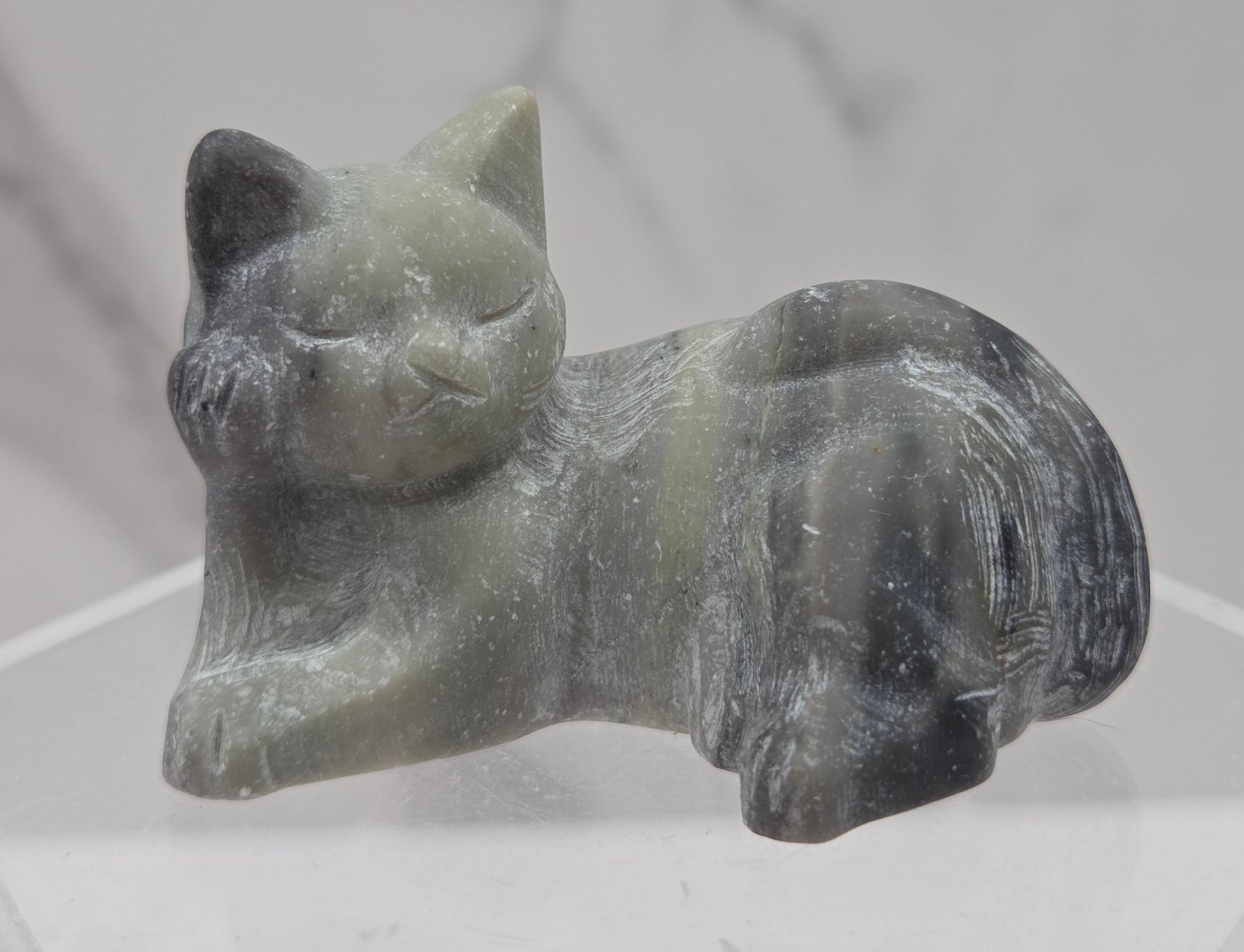 Jasper cat carving lying down an acrylic stand against a neutral background