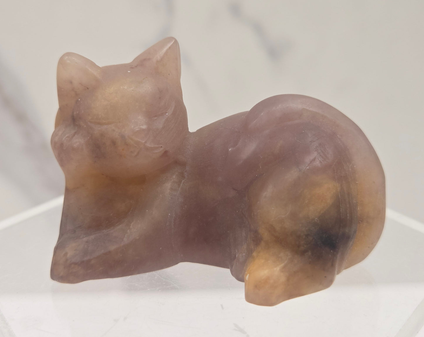 Pink crystal cat carving lying down an acrylic stand against a neutral background