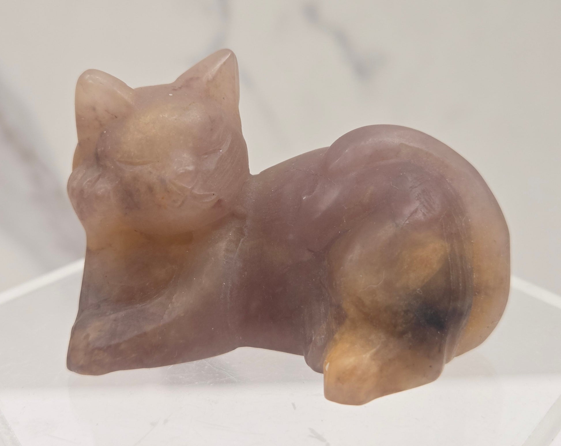Pink crystal cat carving lying down an acrylic stand against a neutral background