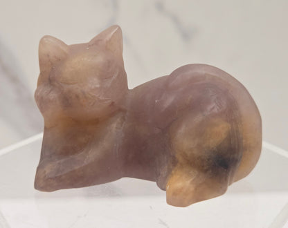 Pink crystal cat carving lying down an acrylic stand against a neutral background